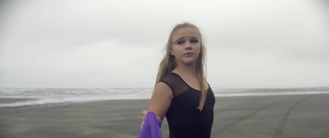 A woman dances on a beach holding a purple piece of fabric