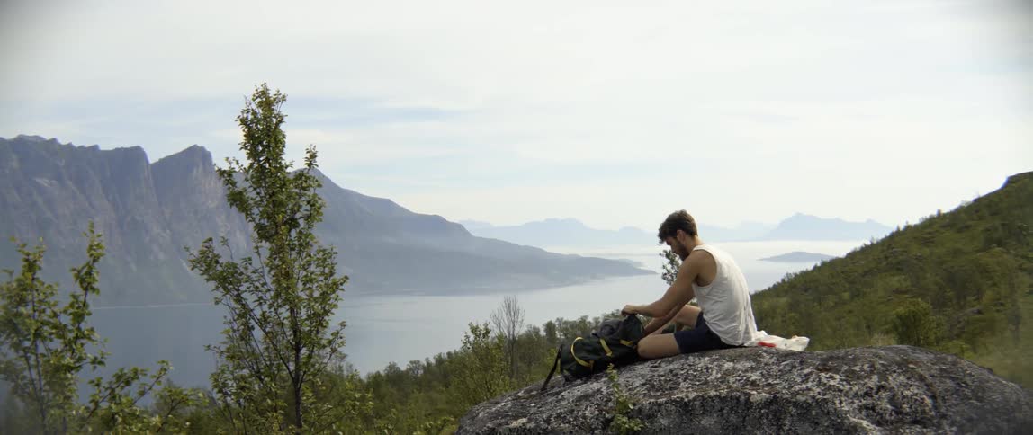 An organized explorer searches through his backpack for supplies during a scenic mountain rest.