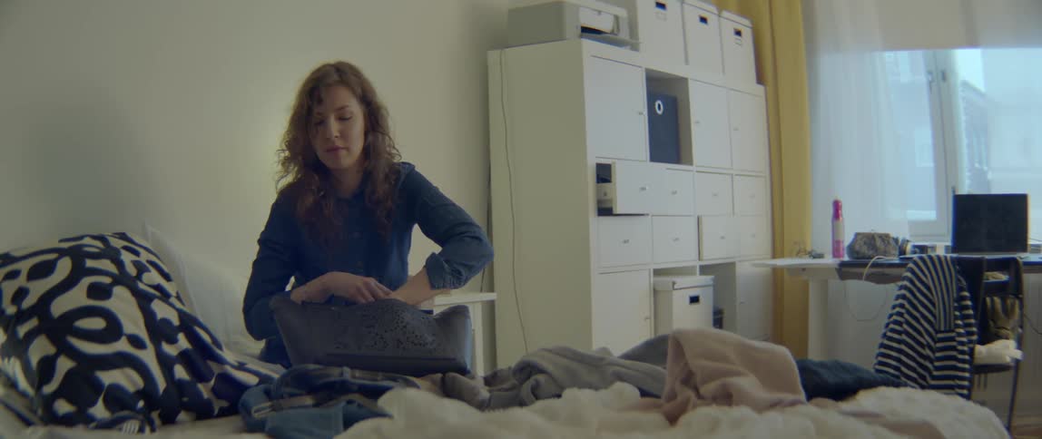 A worried woman looks through her purse for a missing item on a bed.