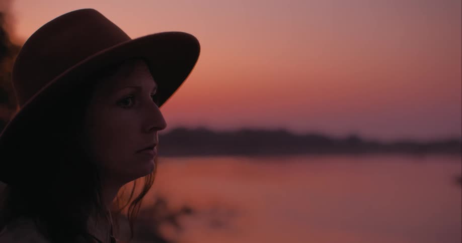 Woman wearing a hat lokks at a lake at sunset