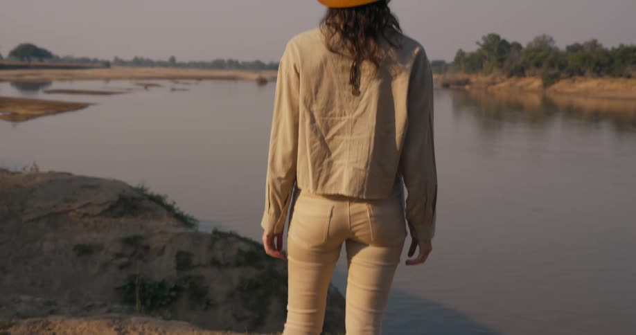 Woman wearing a hat stands next to a lake