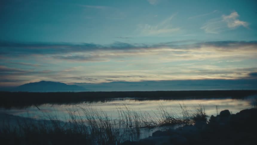 Sky reflected in water framed by reeds at dusk