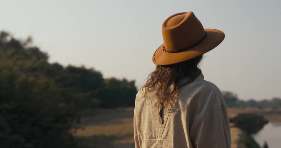 Woman wearing a hat stands next to a river