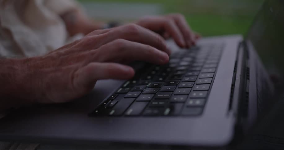 A man is typing on a laptop computer keyboard