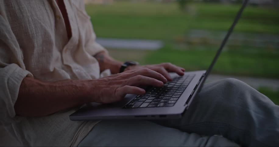 Man typing on laptop sits overlooking valley of flooded fields