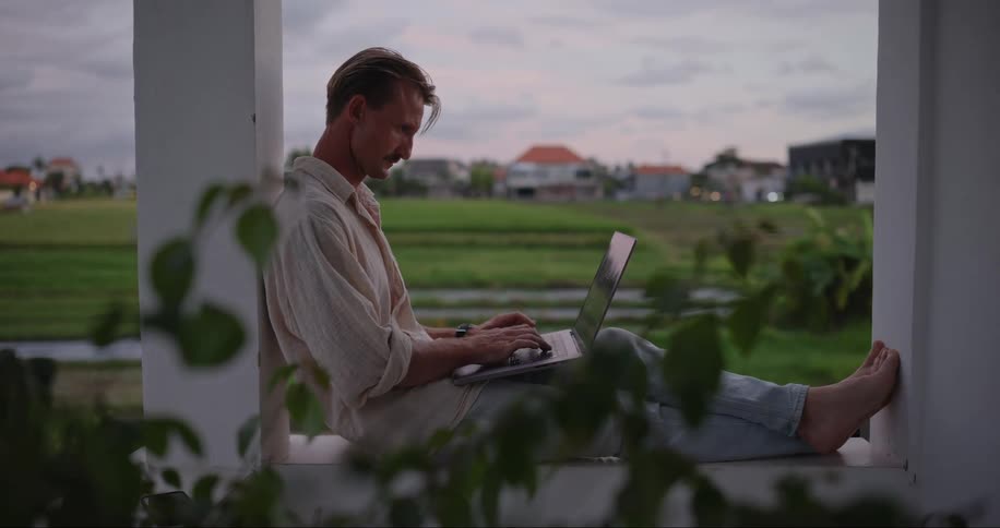 Man sitting on the balcony of a countryside hotel working on a laptop