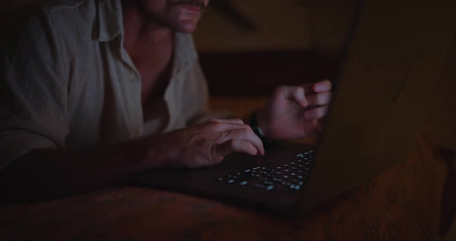 A man working on a laptop lying on the bed in his room