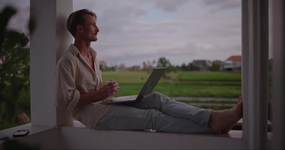 Man sitting on the balcony of a hotel works on a laptop