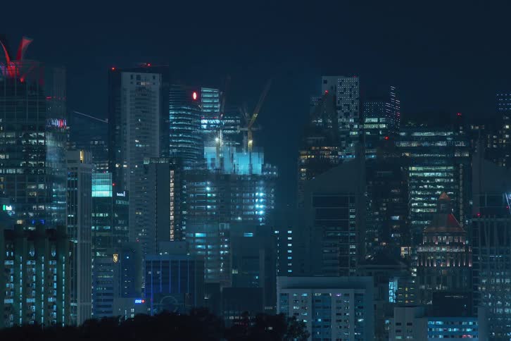 Construction cranes rising over a downtown city is displayed at night