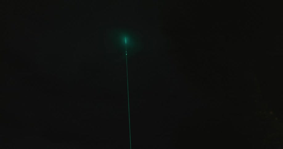Green light on tall narrow pole shines through foggy night near trees
