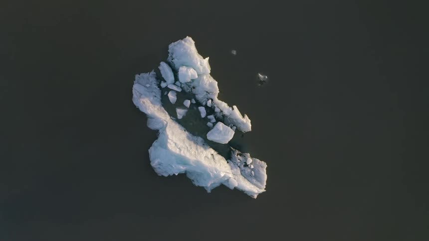 Aerial top view of an iceberg and pieces of ice in dark water