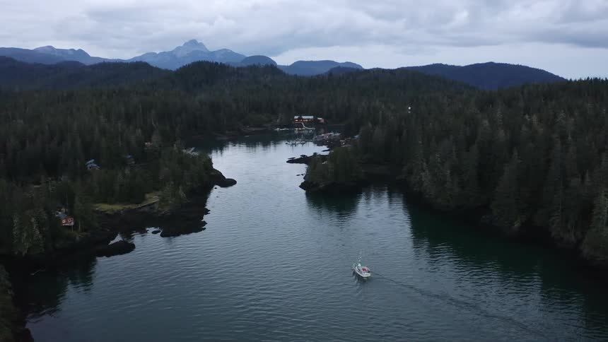 A fishing boat entering a bay with a small town in the mountains