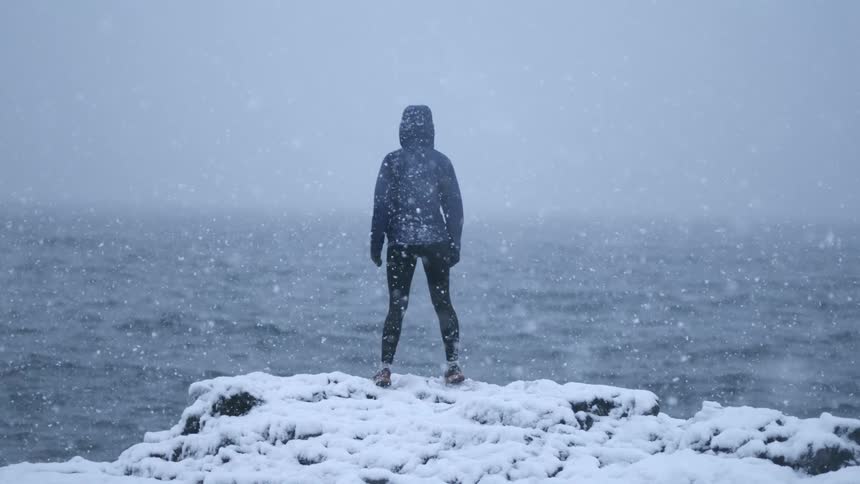 Woman stands in front of the ocean during a snow storm