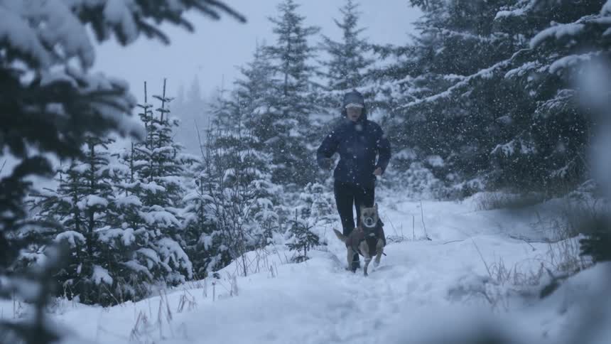 A woman trail running with a dog in the woods during winter