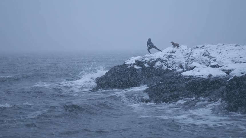 A woman stretching on the coastal rocks during a blizzard