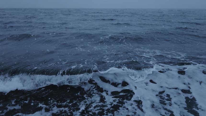 Choppy sea waves while snowing during sunset