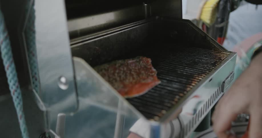 A man roasting fish on a barbecue grill on a boat
