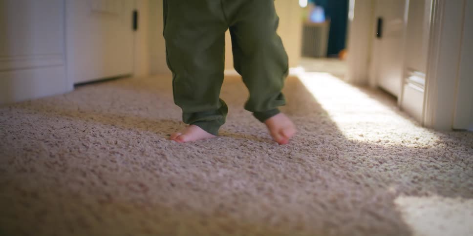 A baby walking on a shag rug in the hallway of the house