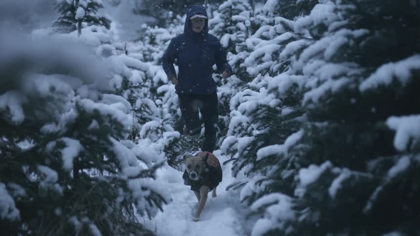 Woman jogs with her dog through the forest at winter