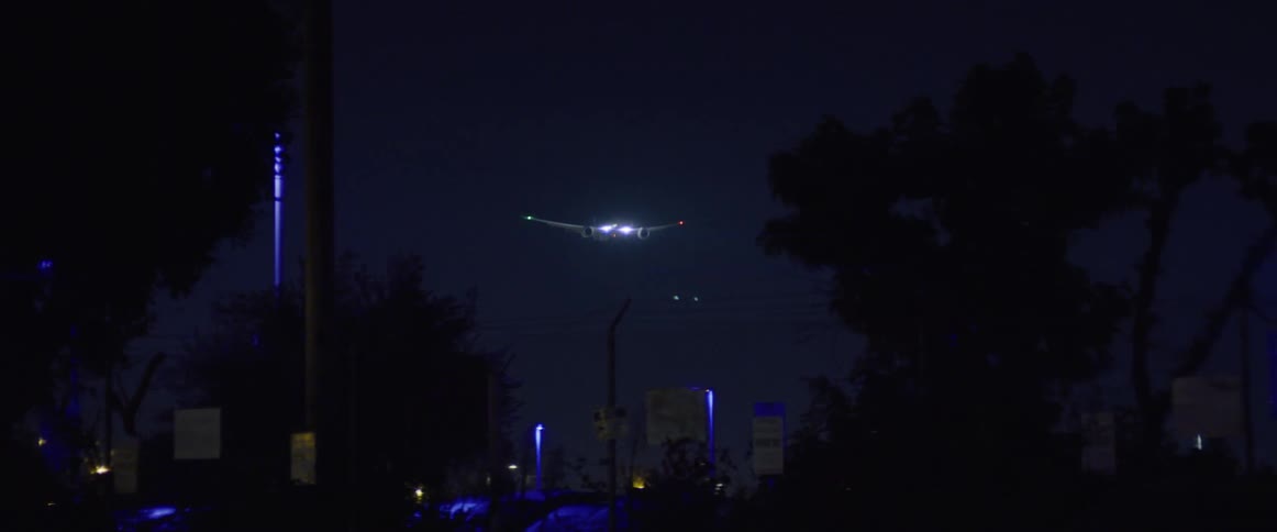 A downtown area in the night with a plane overhead