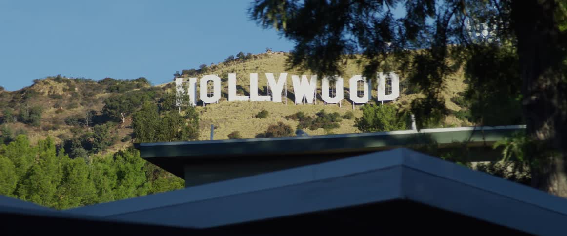 Hollywood sign sitting on hill overlooks houses on a slightly cloudly day