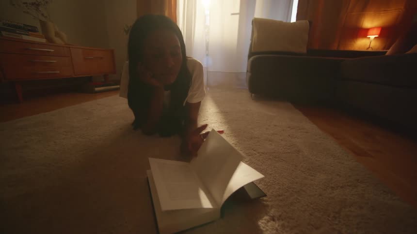 A woman is reading a book on the floor of the living room