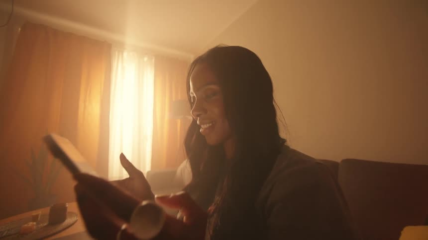 A woman is sitting and looking at a tablet screen and then smiles