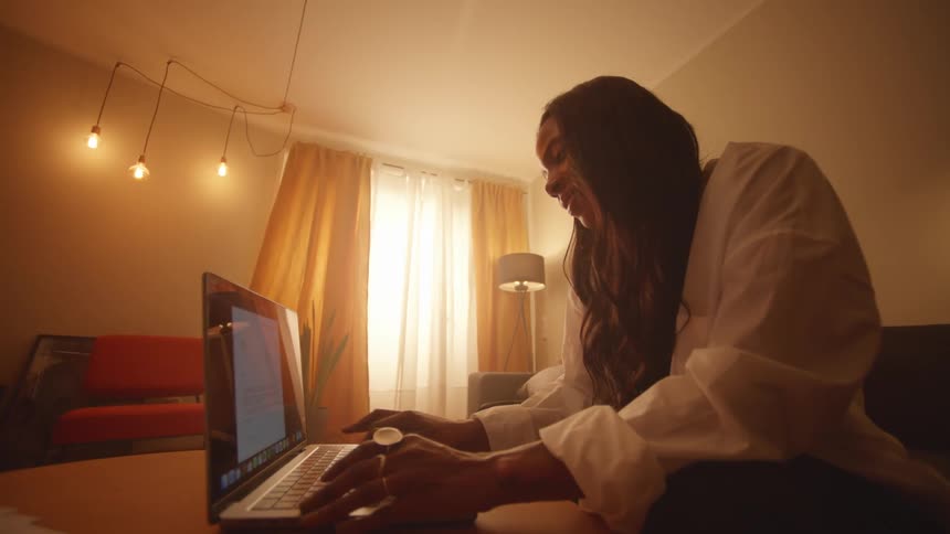Young black woman smiles as she opens her laptop and begins to type