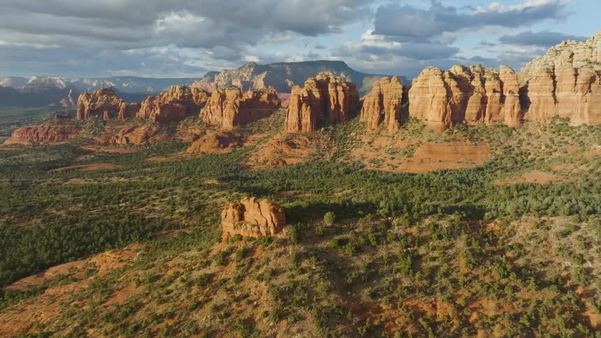 Aerial of green vegetation covered valley leading up to large rock canyon formations under a clouded sky on a bright day