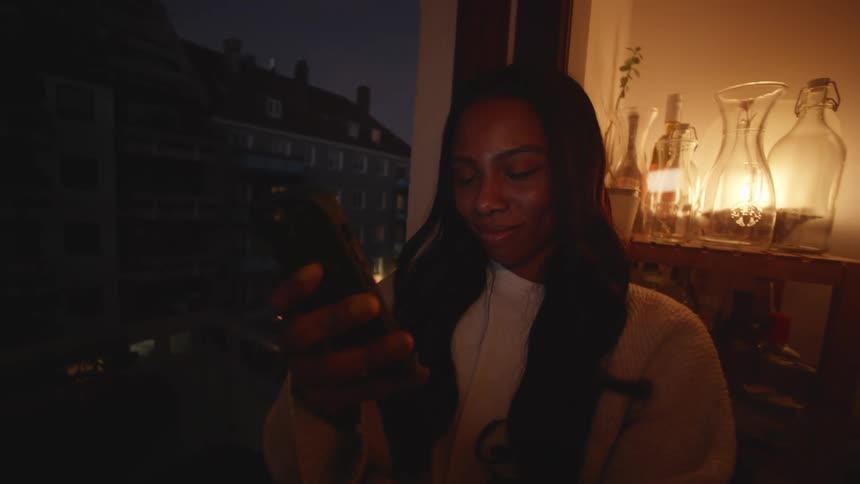 A black female walking down a hallway in a house looking at her phone and smiling
