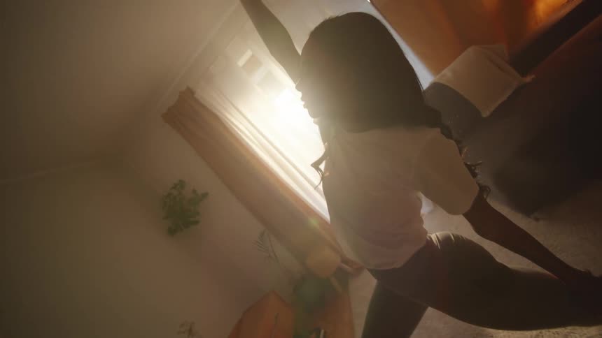 A young woman does a yoga pose while standing in her home