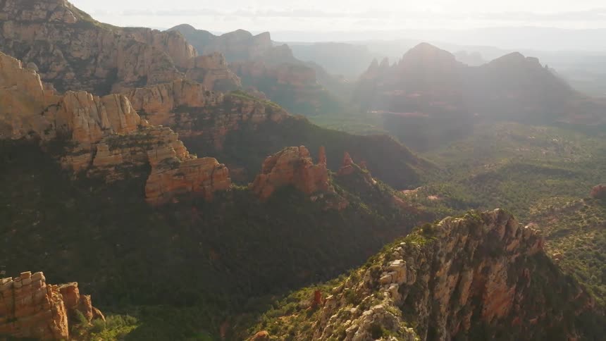 Aerial landscape over vegetation covered valleys between rock canyon formations with the sun glaring the sky in the background