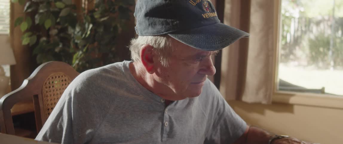 An elderly man is sitting at a desk looking at paperwork
