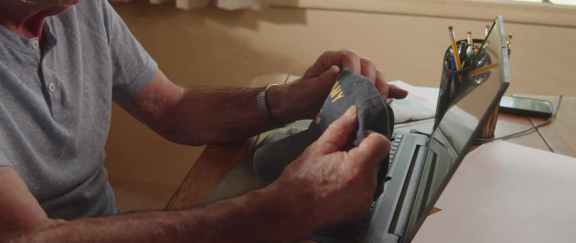 Elderly man working from home looks at his baseball cap