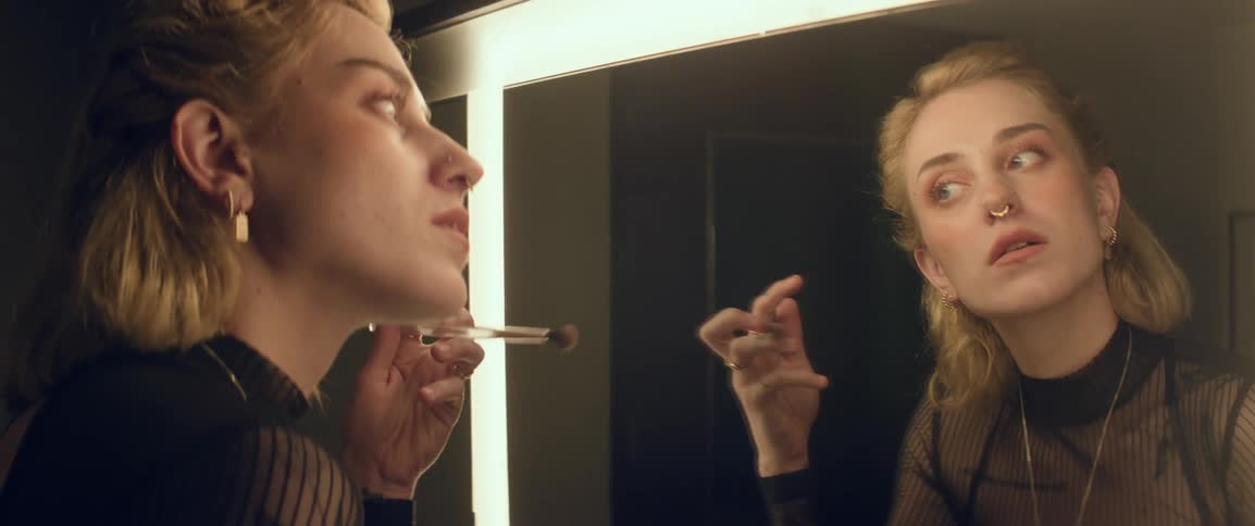 A woman putting on makeup in front of a vanity mirror in her dressing room