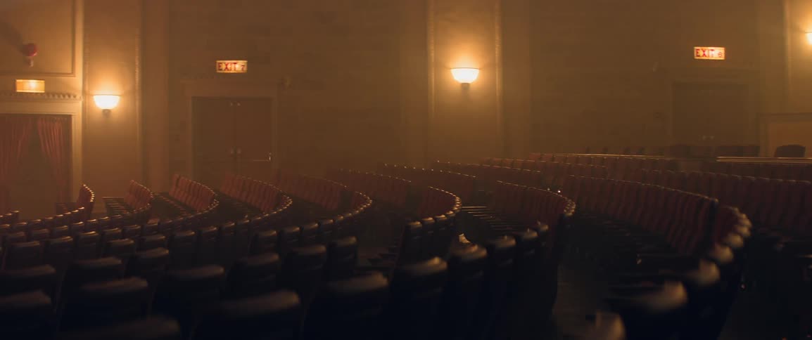 Theater seats form curving rows as the camera sweeps across the room