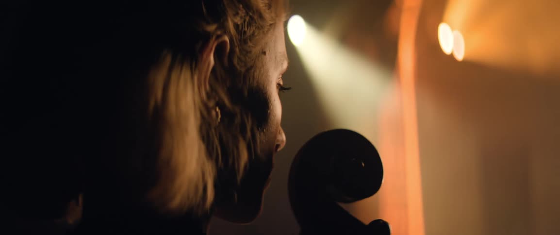 A woman holding a cello waits in the wings before walking onstage to perform