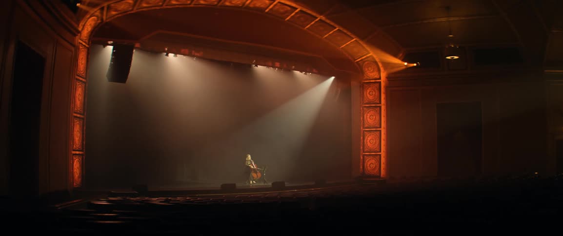 A woman performing classical cello music in the spotlight during a concert