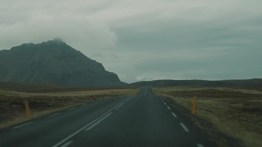 Traveling on a rural road with mountains in the distance under a cloudy sky