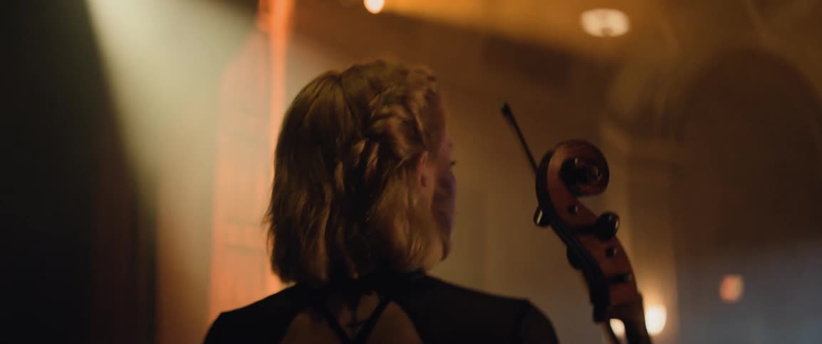 A woman walking onto the stage of a theater with a cello in her hands