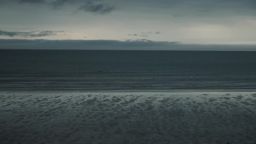 Waves roll into shore and over the frozen beach under a cloudy sky