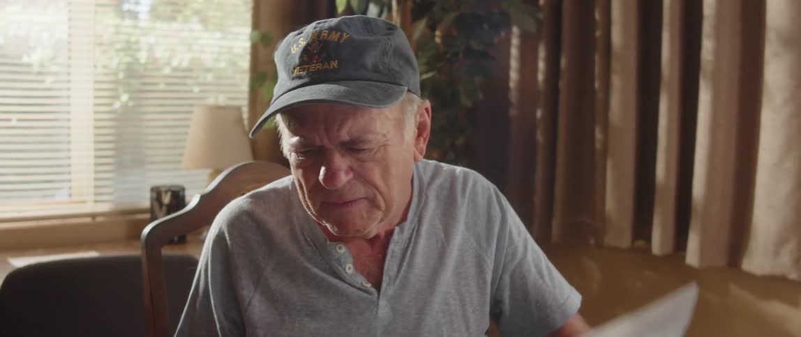 An elderly man is sitting at a table with a laptop computer doing paperwork