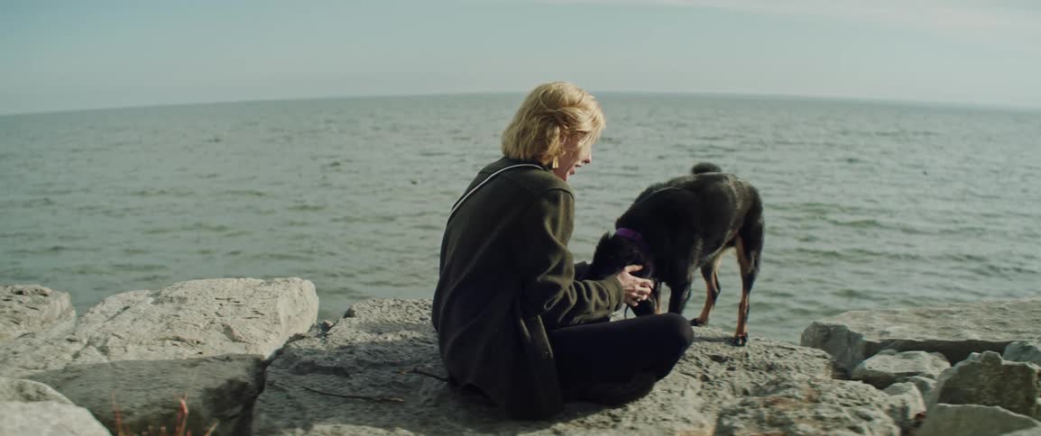 A woman pets her dog on the shore