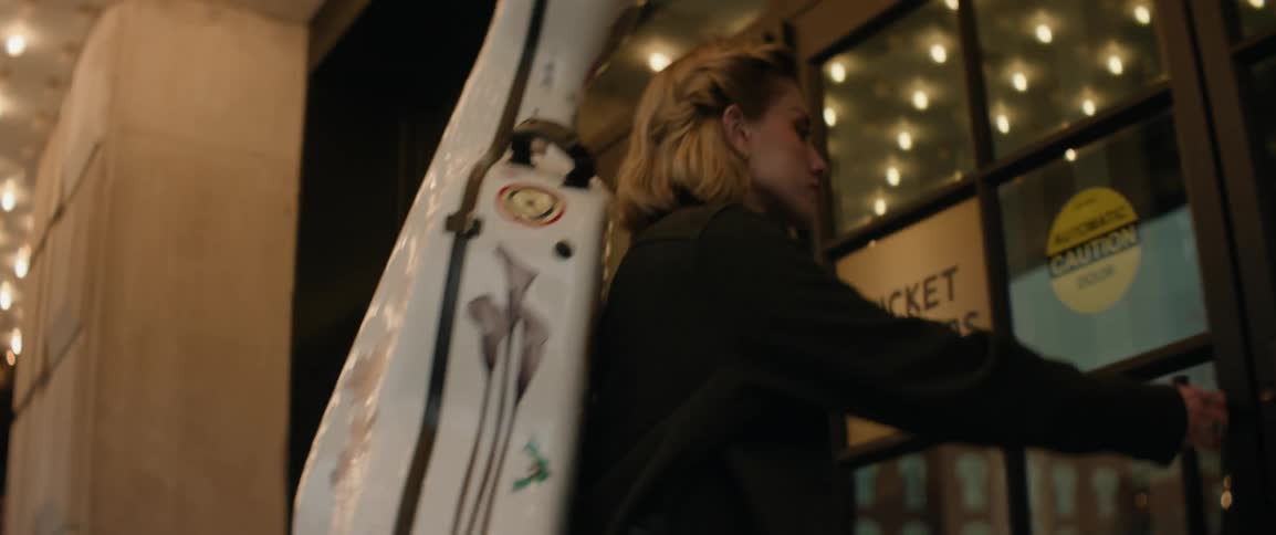 A musician walks under a theater marquee and through the lobby door