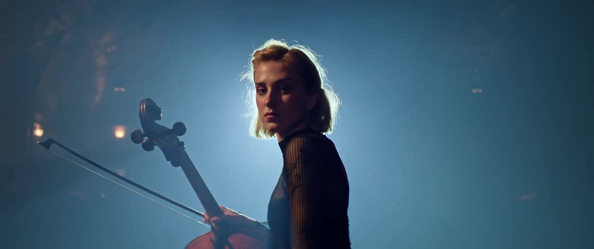 Portrait of a blonde female sitting in a spotlight holding a cello