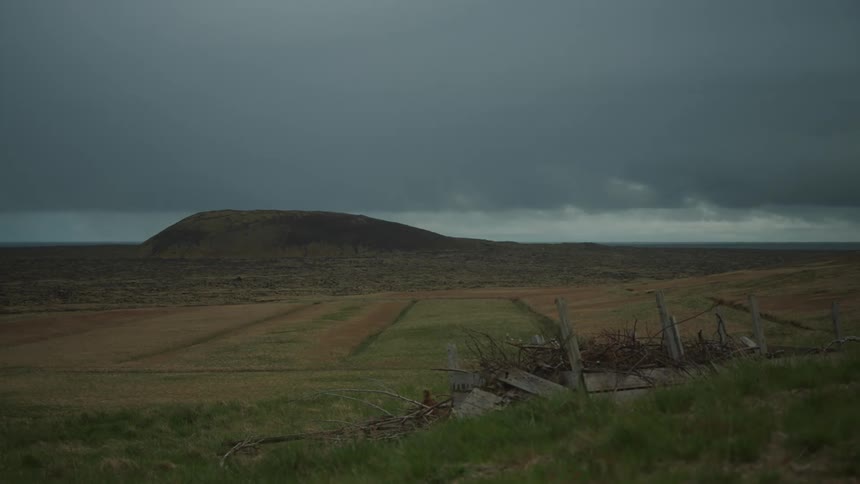 Brush pile in wooden frame sits on hill overlooking fields under dark clouds