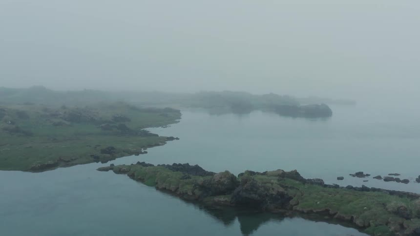 An aerial view of a land surrounded by a sea and with a bit of fog