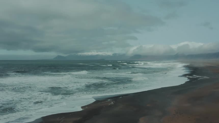 Waves roll into shore and over the beach under a cloudy sky