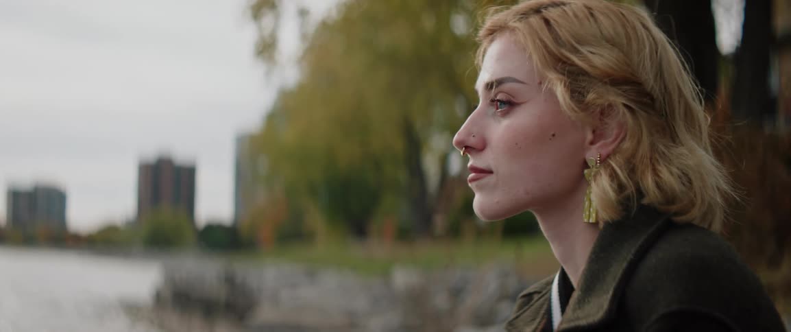 A woman wearing a nose ring is by the lake shore in a city park
