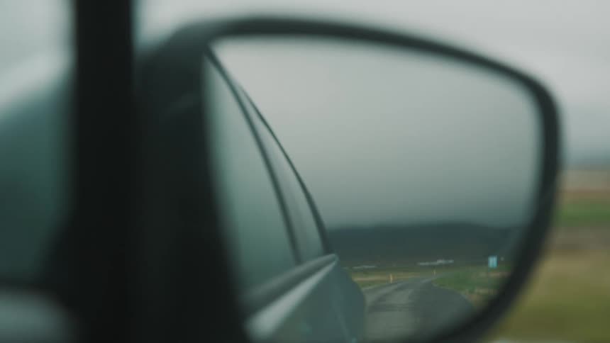 A car driving on a lonely road seen through the side mirror